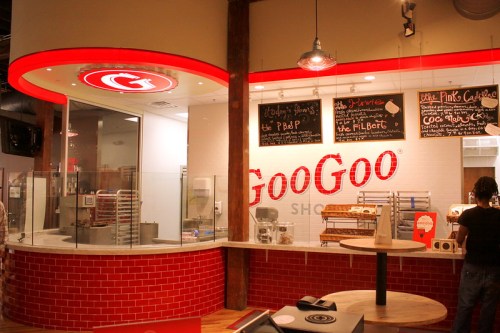Interior of Goo Goo Shop featuring a red and white counter, menu boards, and baking equipment in a modern setting.