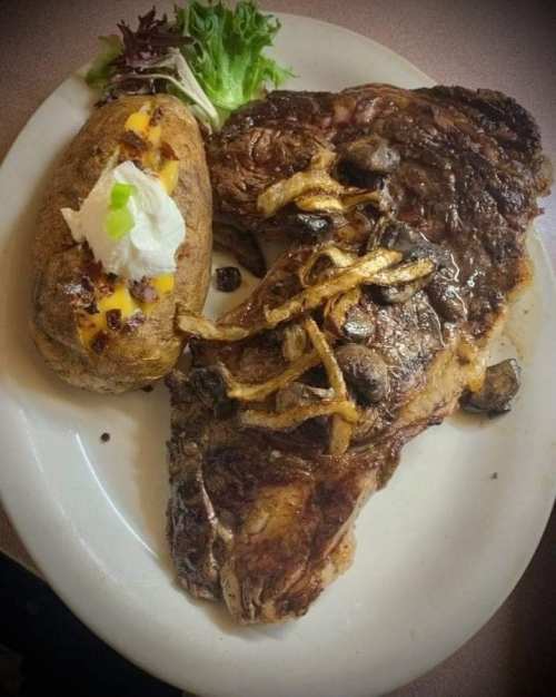 A plate featuring a large grilled steak with sautéed onions, served alongside a baked potato topped with cheese and sour cream.