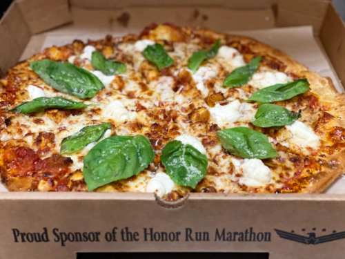 A pizza topped with cheese, spinach, and dollops of white sauce in a takeout box.