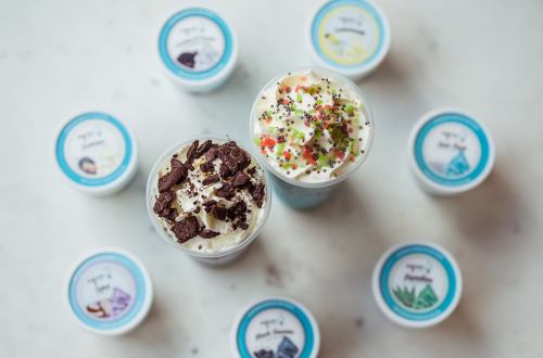 Two colorful dessert cups topped with sprinkles and cookies, surrounded by small containers of various flavors.