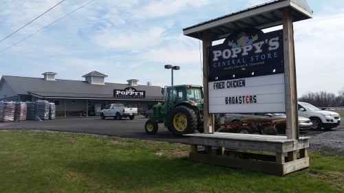 A general store named "Poppy's" with a sign advertising fried chicken, a tractor, and parked cars in front.