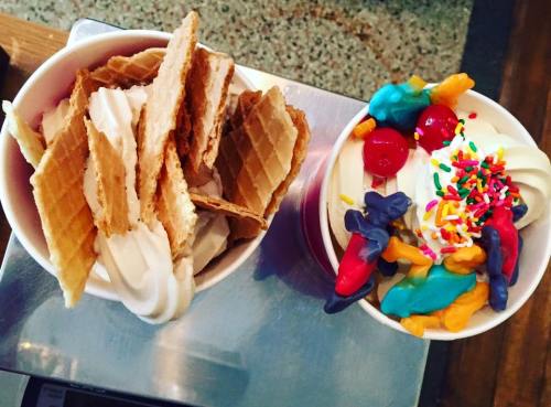 Two cups of soft serve ice cream: one topped with waffle cone pieces, the other with colorful candies and sprinkles.