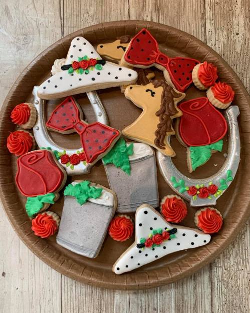 A platter of decorated cookies featuring horseshoes, roses, bows, and a unicorn, all in vibrant colors.