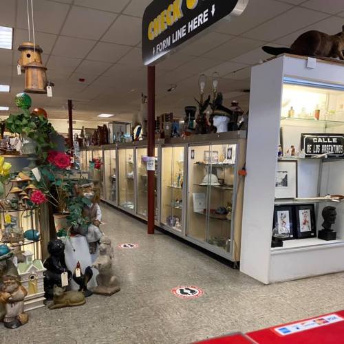 A spacious store aisle with display cases filled with various items, surrounded by decorative plants and sculptures.