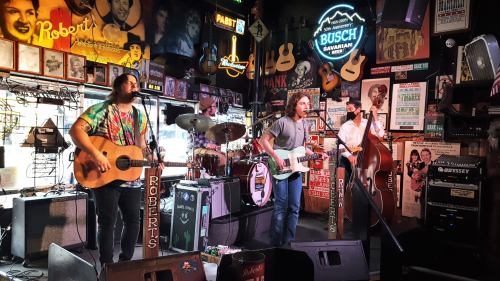 A live band performs in a vibrant bar filled with musical memorabilia, featuring guitars and colorful decor.