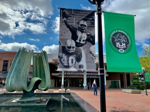 A large sculpture in front of a building, with banners featuring football players hanging nearby against a cloudy sky.