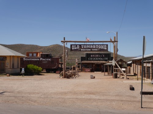 A western town entrance featuring signs for "Old Tombstone" and "Brenda's Chuckwagon," with a vintage train nearby.