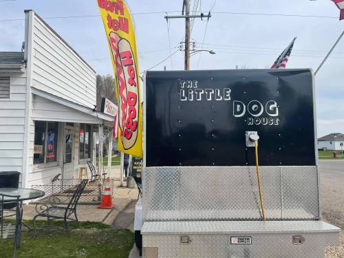 A food truck named "The Little Dog House" parked near a building, with colorful flags and outdoor seating visible.