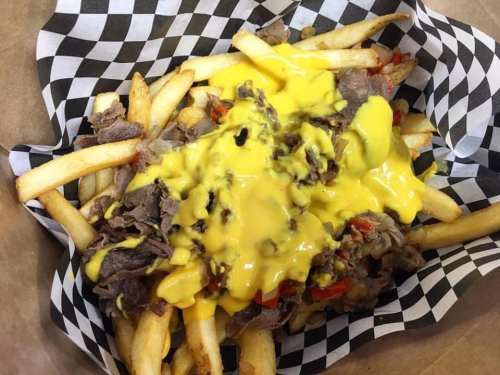 A basket of fries topped with melted cheese, sliced beef, and peppers, served in a checkered paper liner.