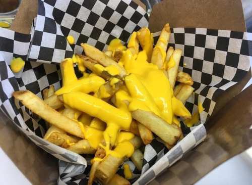 A basket of golden French fries topped with melted cheese sauce, served in a black and white checkered paper.