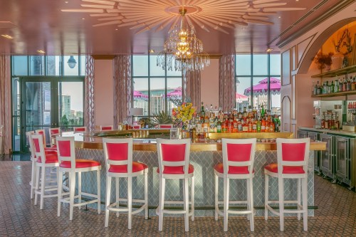 A stylish bar with pink and white decor, featuring a chandelier and a variety of colorful bottles on the shelves.