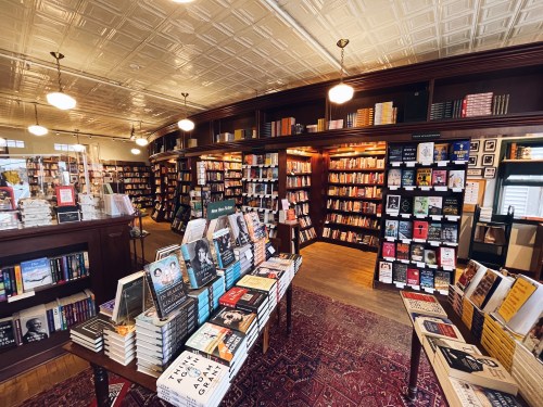 A cozy bookstore interior with wooden shelves filled with books and a display of titles on a table in the foreground.