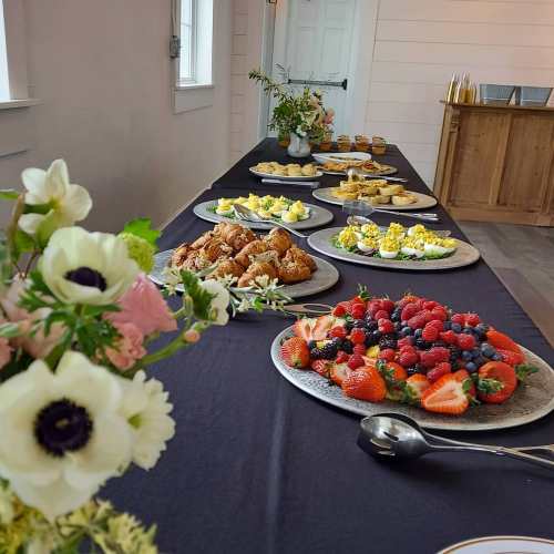 A beautifully arranged table with various dishes, including pastries, fruit, and desserts, surrounded by floral decorations.