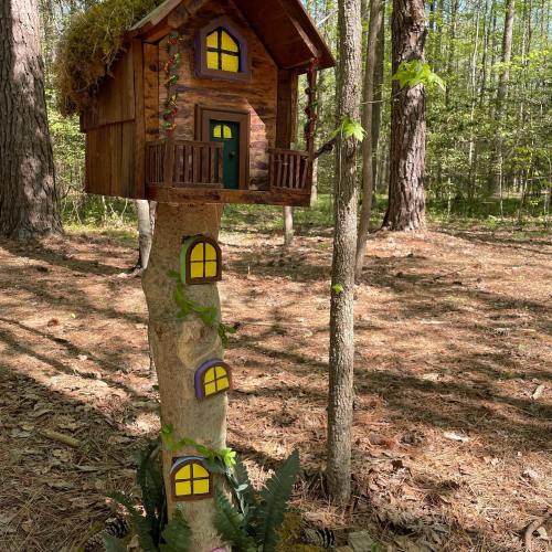 A whimsical treehouse perched on a tree trunk, surrounded by greenery and sunlight in a forest setting.