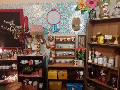 A cozy vintage shop display featuring shelves of decorative items, teacups, and colorful wall decor.