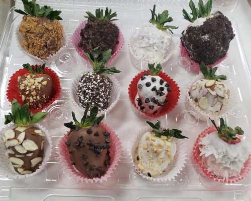 A tray of 12 decorated strawberries, coated in various toppings like chocolate, nuts, and coconut, in colorful liners.