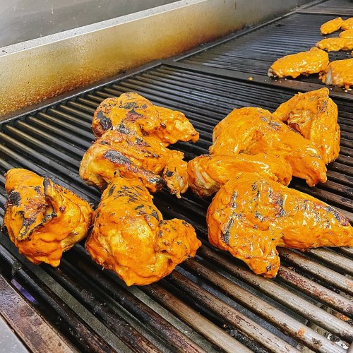 Grilled chicken pieces coated in orange marinade on a barbecue grill.
