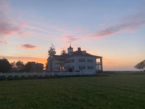 A large, elegant house at sunset, with a colorful sky and a green lawn in the foreground.