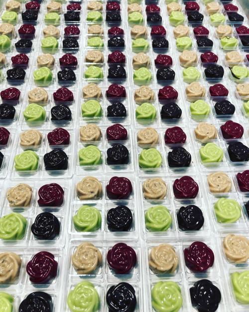 A colorful array of small, rose-shaped candies in green, red, black, and beige, arranged in a grid pattern.