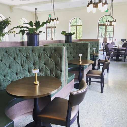 A stylish café interior featuring green upholstered booths, round tables, and elegant lighting.