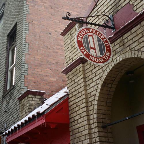 Sign for "Bookpeople of Moscow" hanging from a brick building, with snow on the roof and a red awning below.