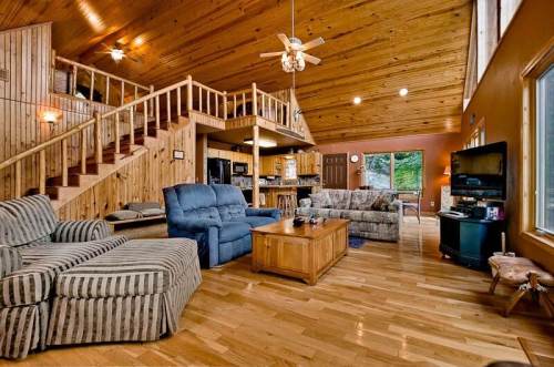 Cozy wooden living room with high ceilings, comfortable seating, and a staircase leading to an upper level.
