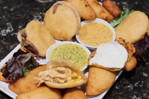A platter of various stuffed arepas with dipping sauces, garnished with lettuce.