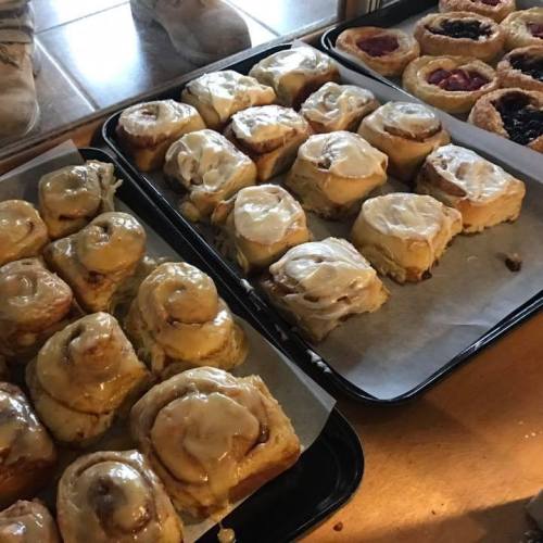 Freshly baked cinnamon rolls with cream cheese frosting on trays, alongside fruit pastries.