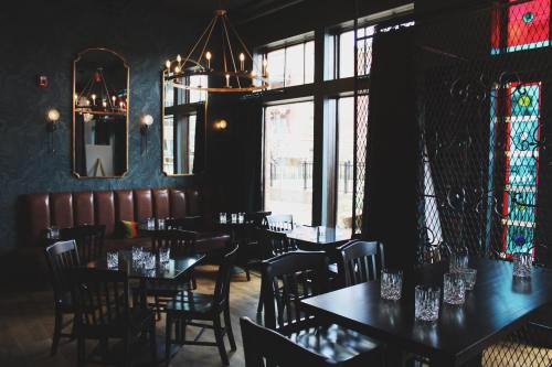 A stylish restaurant interior featuring wooden tables, chairs, and large windows with decorative lighting and stained glass.