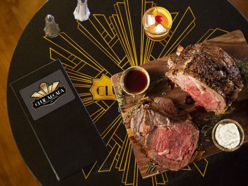 A beautifully plated prime rib roast with sides, a menu, and a cocktail on a stylish table.