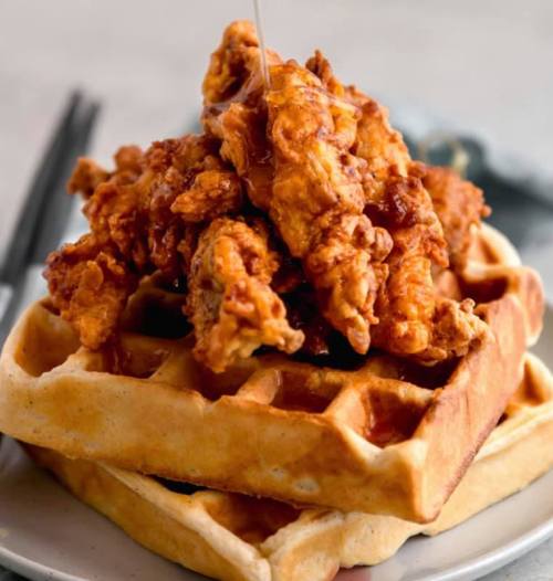 A stack of waffles topped with crispy fried chicken and drizzled with syrup.