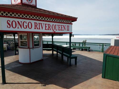 A dock with a gazebo labeled "Songo Riverqueen II" overlooking a frozen river and distant hills.