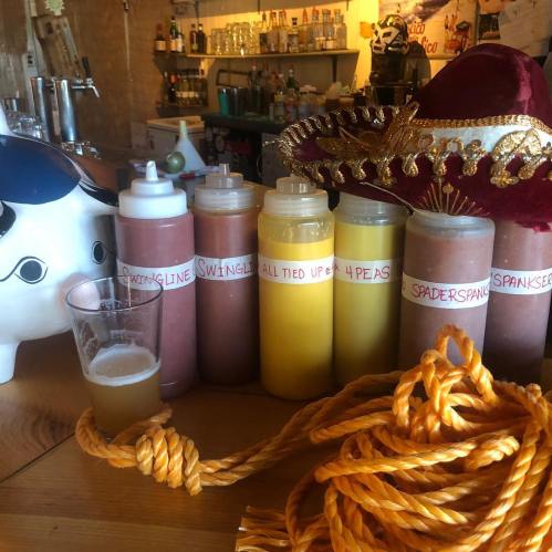 A bar scene featuring colorful drink bottles, a glass of beer, a decorative hat, and a rope on a wooden table.
