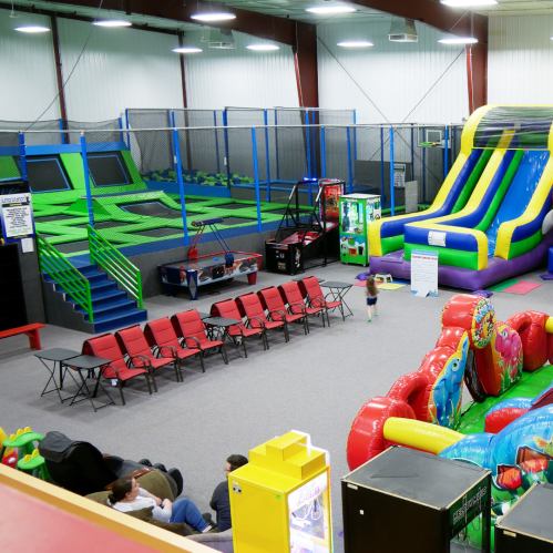 Indoor play area featuring trampolines, inflatable slides, arcade games, and seating for visitors.