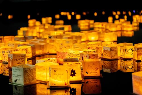 A serene scene of glowing paper lanterns floating on water, each adorned with handwritten messages and drawings.
