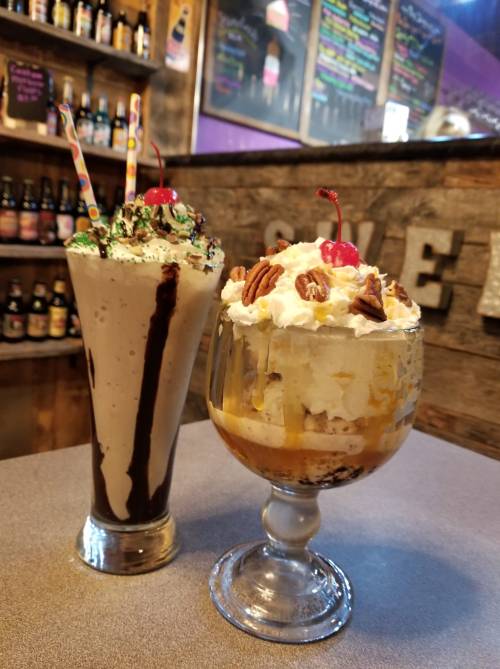 Two delicious desserts: a chocolate milkshake with whipped cream and a sundae topped with nuts and a cherry.
