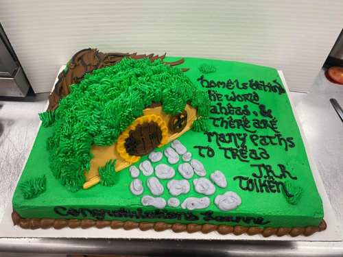 A colorful cake featuring a hobbit house, grass, and a quote from J.R.R. Tolkien, celebrating "Congratulations, Lauren."