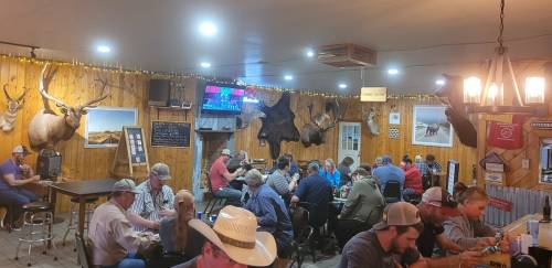 A lively restaurant interior with patrons dining, rustic decor, and mounted animal heads on wooden walls.