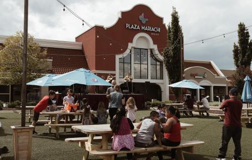 A lively outdoor scene at Plaza Mariachi with musicians performing on stage and families enjoying the space.