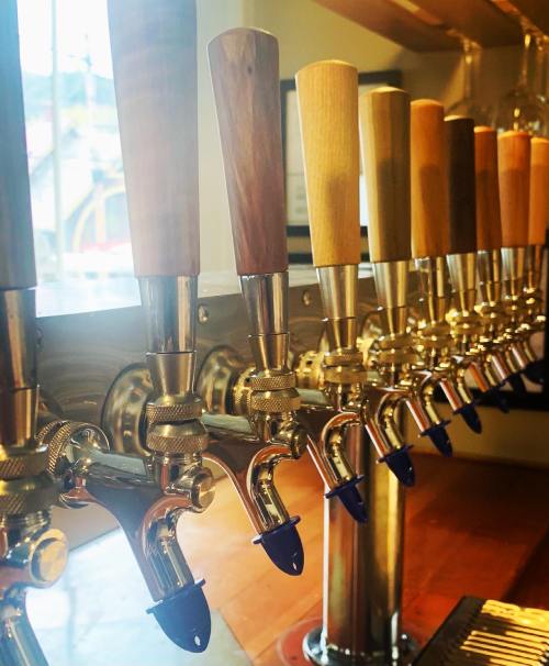 A row of beer taps with wooden handles, lined up on a bar counter, with natural light in the background.