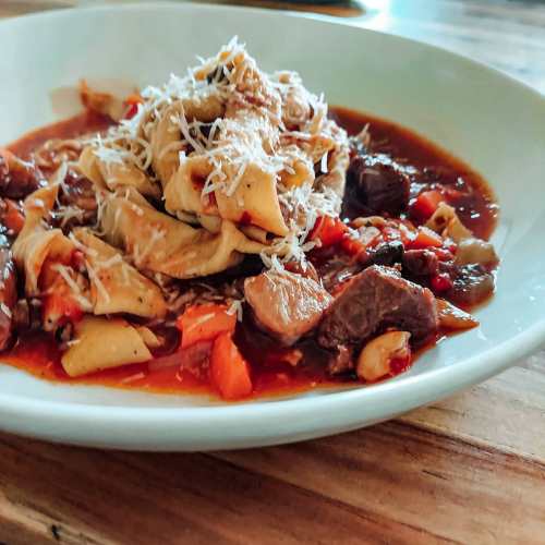 A plate of hearty pasta topped with shredded cheese, surrounded by a rich meat and vegetable sauce.