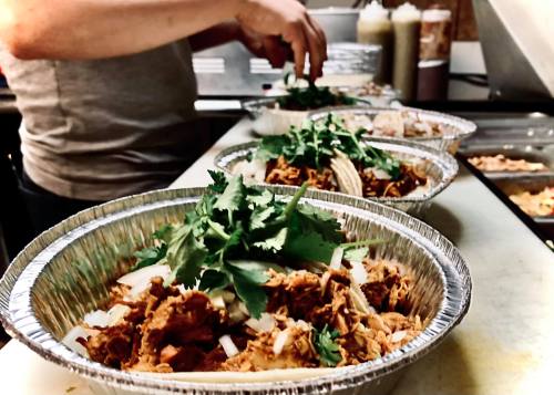 A person prepares bowls of food topped with cilantro in a kitchen setting.