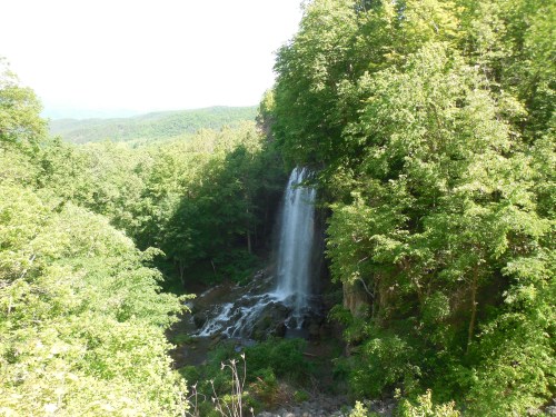 A serene waterfall cascading down rocky cliffs, surrounded by lush green trees and a mountainous landscape in the background.