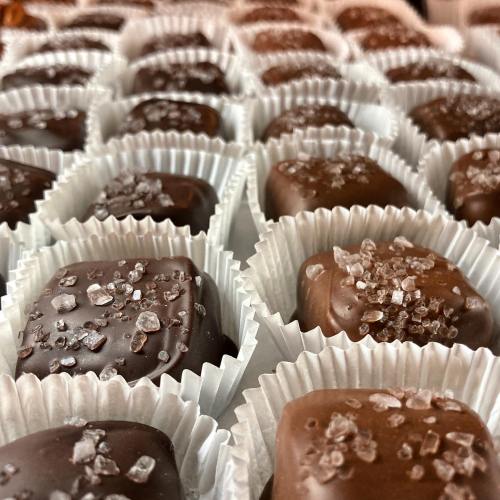 A close-up of assorted chocolate candies topped with coarse salt, arranged in white paper cups.