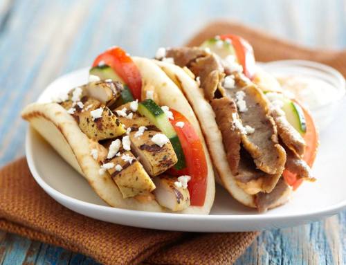 Two pita sandwiches filled with grilled chicken, beef, tomatoes, cucumbers, and feta cheese on a white plate.