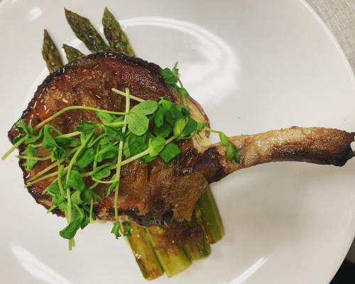 A beautifully plated pork chop topped with microgreens, served on a bed of asparagus.