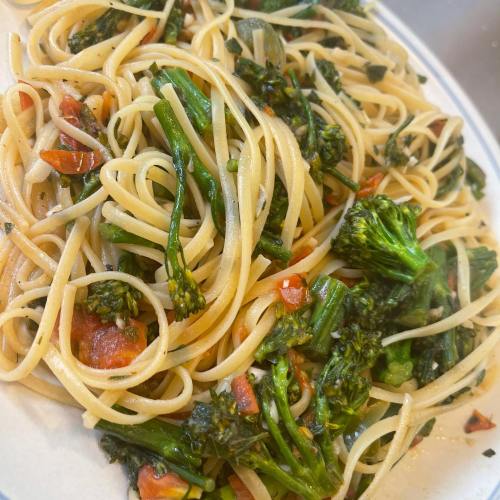 A plate of spaghetti tossed with broccoli, tomatoes, and herbs, garnished with olive oil and pepper.