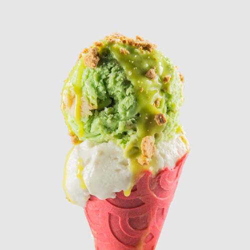 A colorful ice cream cone with green and white scoops, topped with a drizzle and crushed toppings.