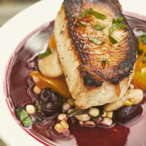 A beautifully plated dish featuring seared fish atop a vibrant berry sauce, garnished with herbs and accompanied by vegetables.