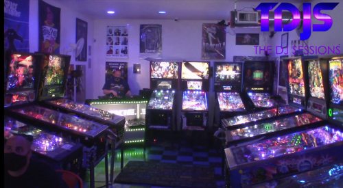 A vibrant arcade with multiple pinball machines and a DJ setup, featuring colorful lights and posters on the walls.